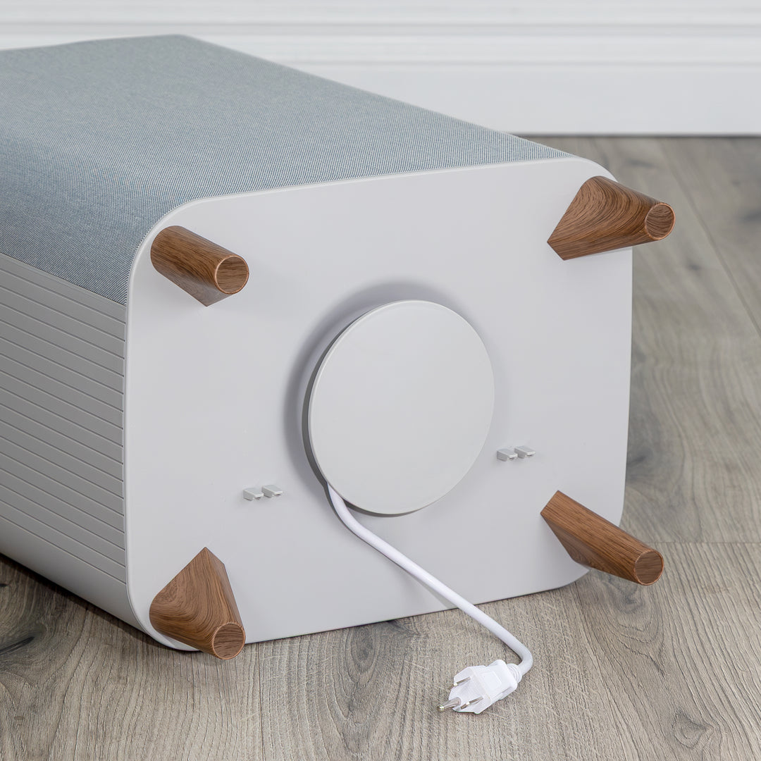 Bottom of gray towel warmer's white electronic cord wrapped around storage compartment with wooden legs on a wooden floor