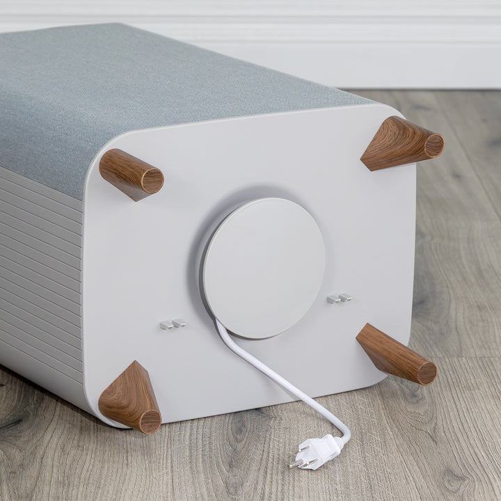 Bottom of gray towel warmer's white electronic cord wrapped around storage compartment with wooden legs on a wooden floor