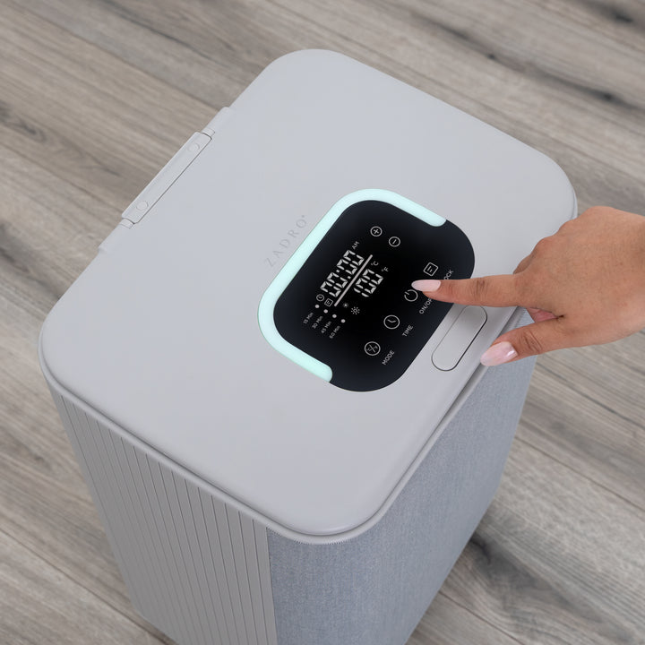 Gray towel warmer with digital display on a wooden floor and a woman's hand touching the control panel on gray wooden bathroom floor