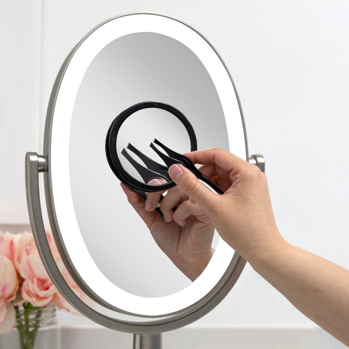 Zadro EZG12LT9 705004420662 environment photo in use hand holding tweezers up to mirror, compact mirror with magnification & lighted tweezers in front of a real life setting