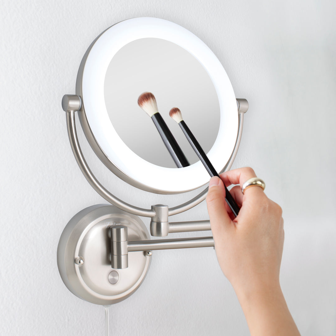 Zadro SLWRLT410 705004423441 in-use photo side view hand holding brush to magnified mirror , lexington lighted wall mounted makeup mirror with magnification in a real life setting